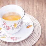 Tazza di tè fumante su un tavolo, con fette di limone e foglie di tè fresche.