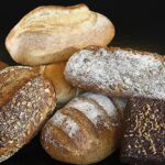 Fette di pane su un tavolo con misurini e alimenti sani, per illustrare il consumo moderato di pane.